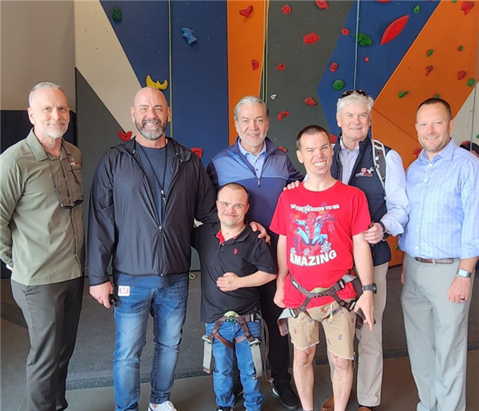 seven men standing behind a rock wall at a ServiceSource event